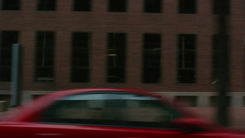 Moving on a street as cars are parked outside of buildings and also on the street and trees are near the sidewalks in town