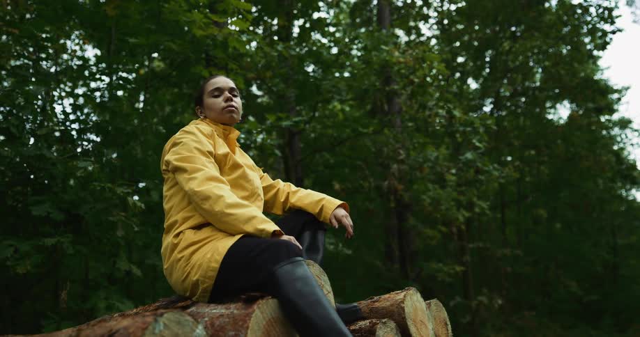 A woman is sitting on a stack of logs by the forest