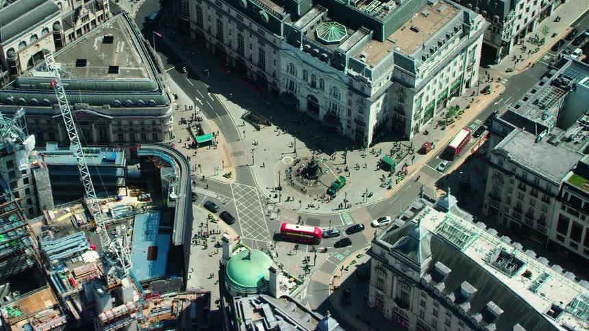An aerial view of vehicles driving and people walking in a city past office buildings and construction cranes