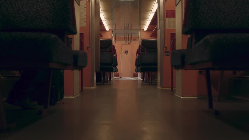 Shoes of person sitting in train seat with luggage is illuminated as light shines into train car windows