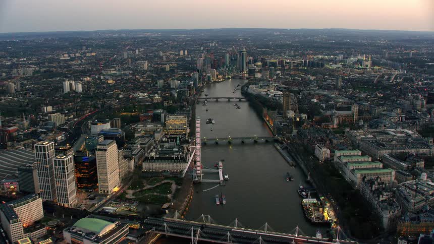 Ferris wheel stands near busy river strewn with boats in large city