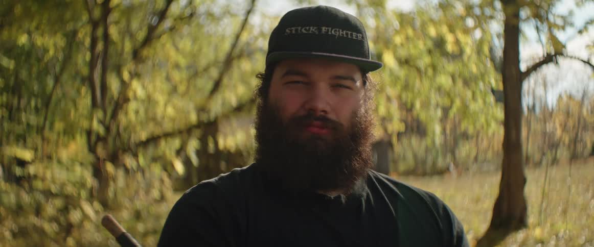 Close up of the face of a bearded man standing in the countryside looking at the camera