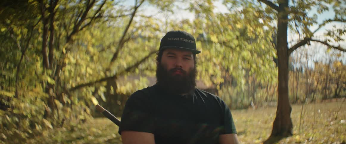 A portrait of a man with a beard standing outside near trees in autumn