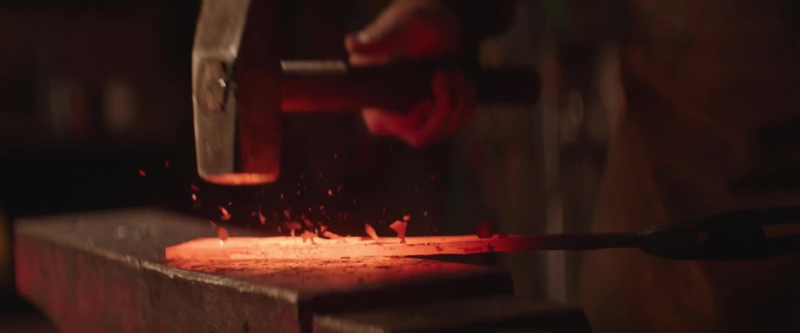 Blacksmith hammers glowing hot metal on anvil