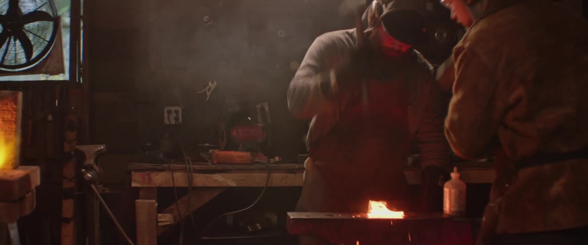 Two blacksmiths striking hammers on hot metal material on their anvil