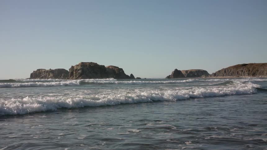 Small ocean waves gently crashing in the coast next to rock formations in the morning