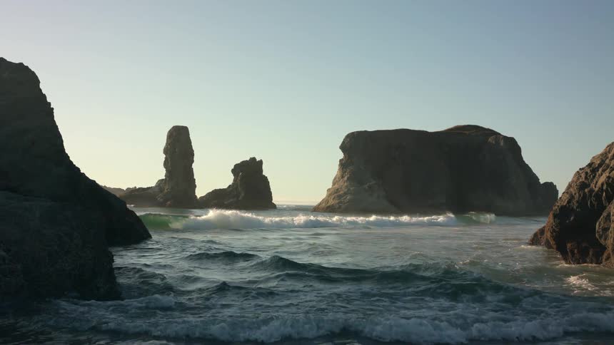 Small ocean waves gently crashing in the coast next to rock formations in the morning