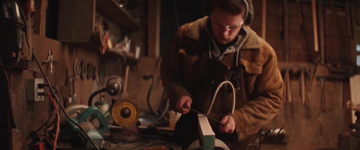 Carpenter trims the edges of a plank of wood in the workbench in his workshop