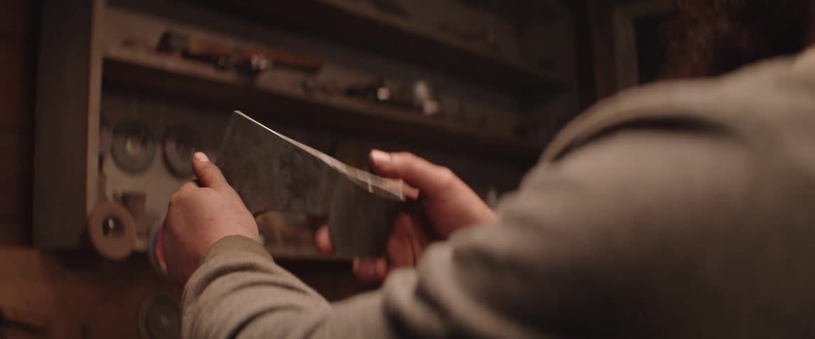 A man holding and turning an axe head in his hands that he has forged in his workshop