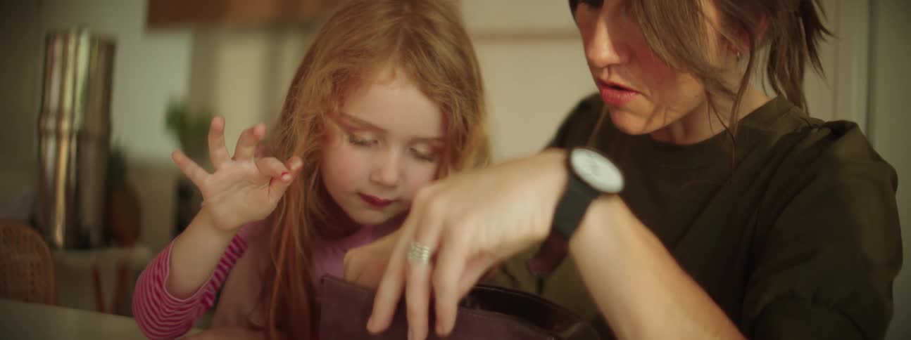 A little girl watches her mother as she picks up a make up brush