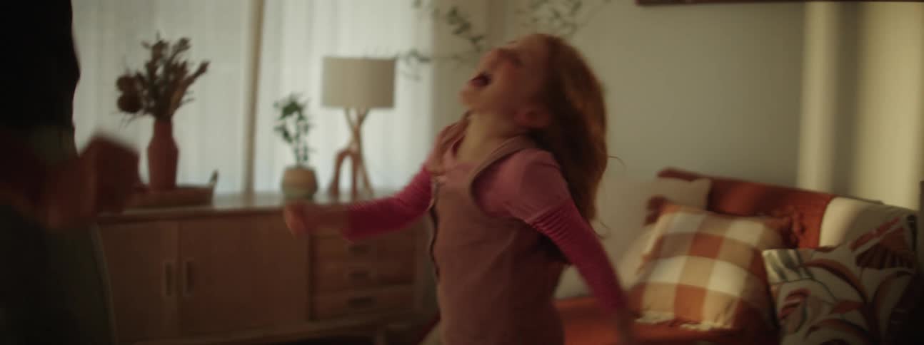 A girl and her father laugh while dancing around their living room