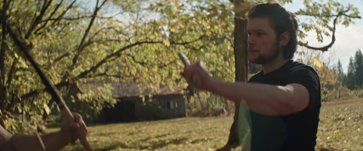 Two men rehearse stick fighting in a rural field area