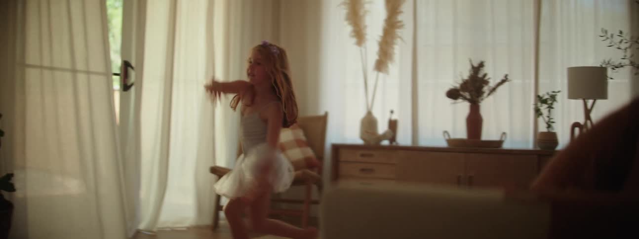 A girl dressed as a ballerina playfully dances in the living room of a house during the day