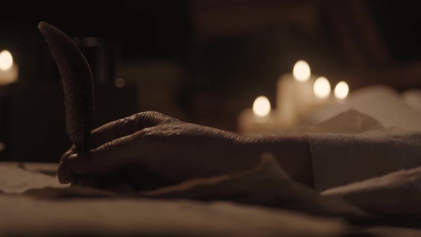 A man is writing with a feather by candlelight