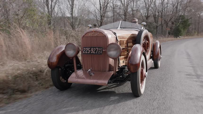A vintage car drives down a small road