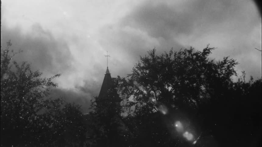 Looking through a rain covered window a cross stands tall on top of a church as dark clouds move across the sky