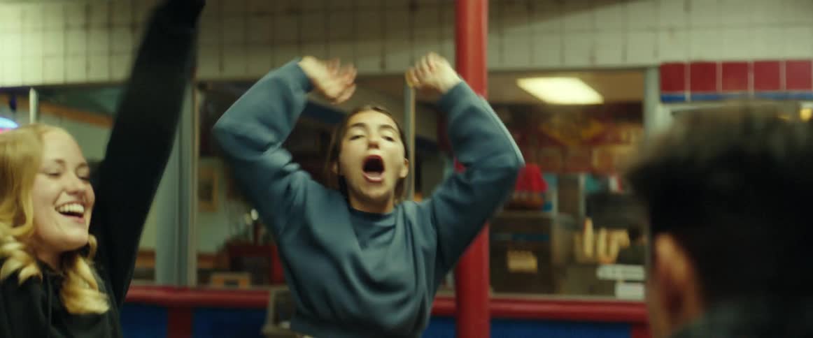 Girl with sweater and ripped jeans throws food in boy's mouth laughing in front of restaurant