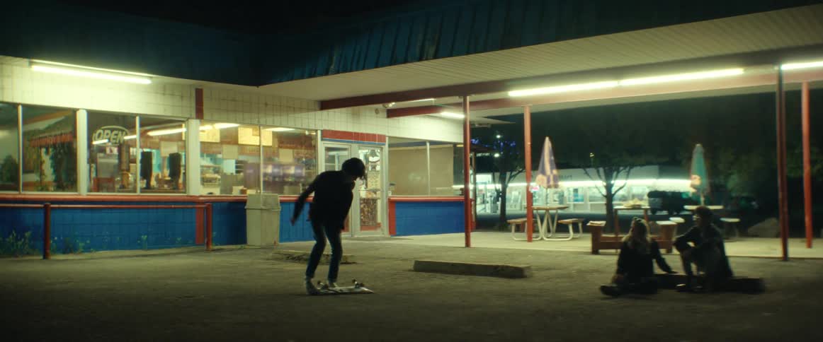 Teen boy practices skateboard trick outside of a diner at night