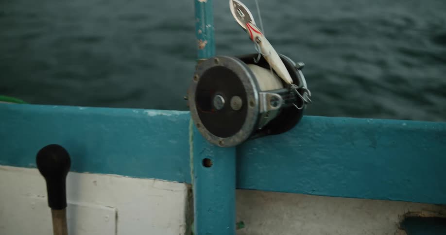 Close up of the reel and lure attached to a fishing rod on the side of a boat in the ocean
