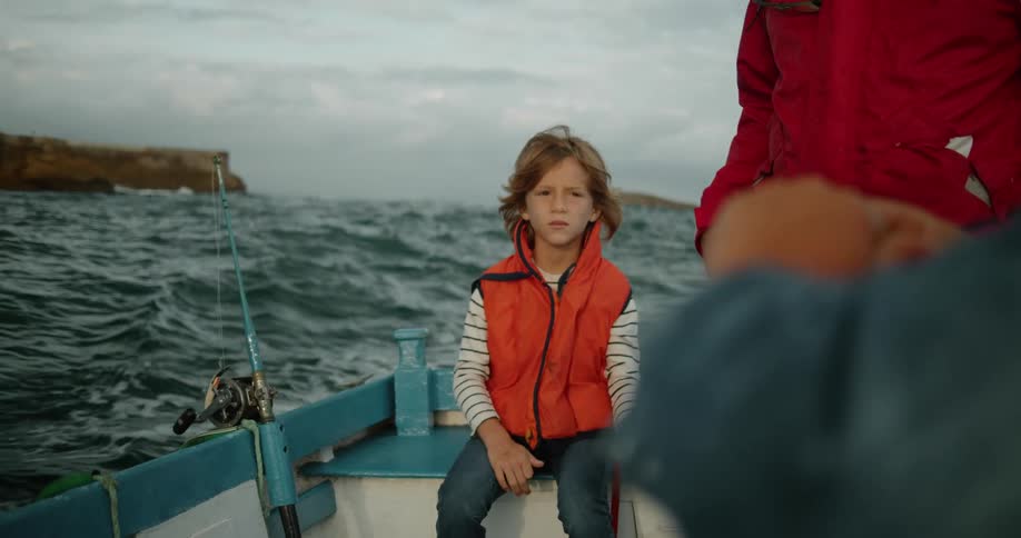 A boy sits on a boat next to his standing father