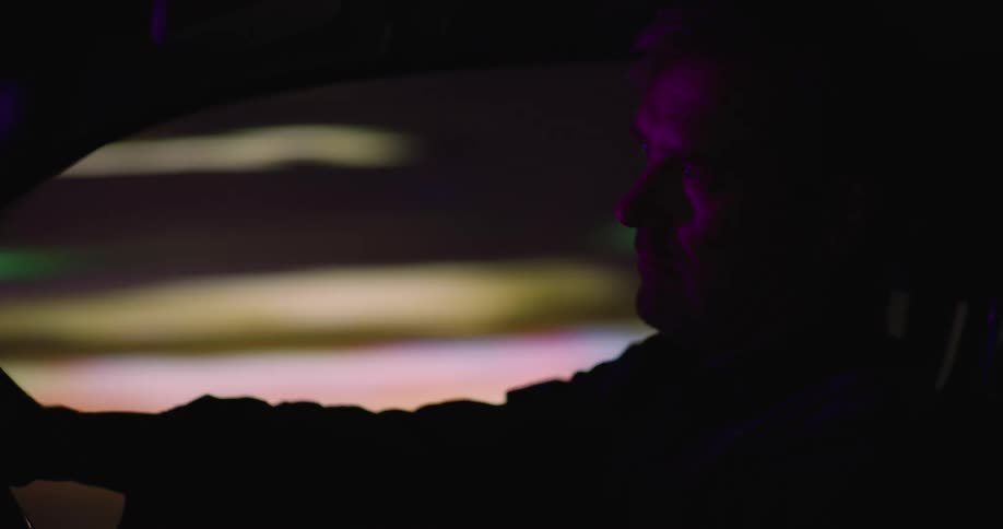 Side profile of man wearing jacket driving car in illuminated city street at night