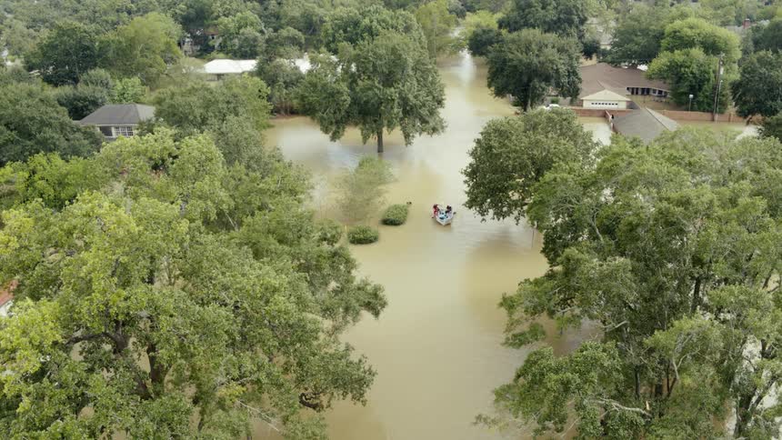 A group of people paddle a boat through a flooded residential neighborhood during the day