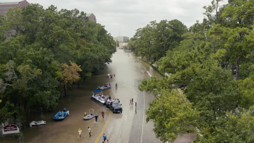 People with boats and people standing in a flooded area on a road