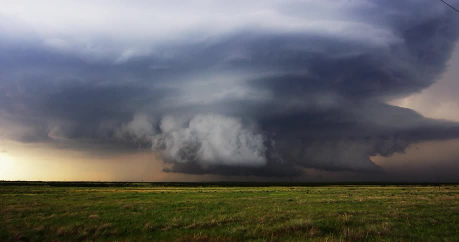 Landscape of green meadow and distant dark clouds gathering in the sky