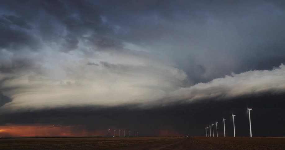 Turbines spin wildly as lightning strikes and dark storm clouds move over a wind farm