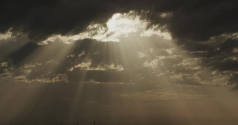 Rays of sunlight shine through a dark cloudy sky