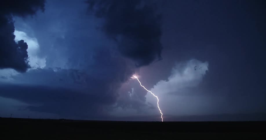 Lightning strikes through dark clouds over a field