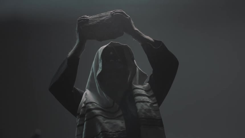 A man lifts a large rock overhead and swings it downward