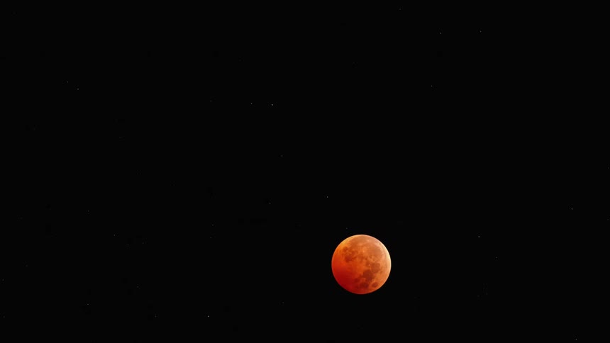 An orange hued moon moves south in the sky