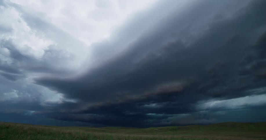 Dark clouds move over an open field as lightning flashes inside the storm clouds