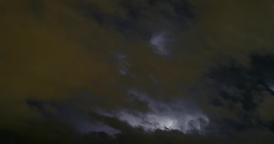 Lightning flashes brightly in the night sky above the clouds