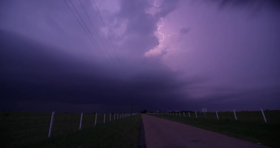 Lightning flashes in dark storm clouds over a countryside road at night