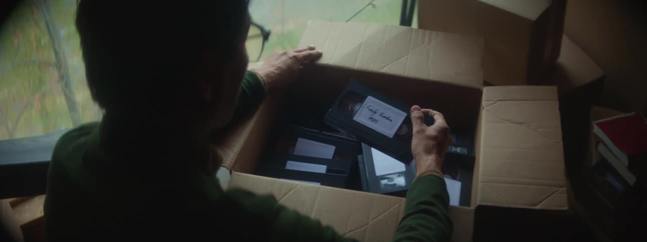 Man opens cardboard box to examine labeled vcr tapes