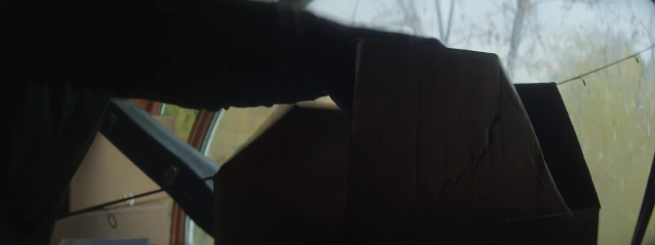 Man with glasses and green sweater opens box and takes a tape out in the attic