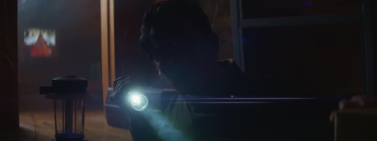 A man looks around a dark room with a flashlight