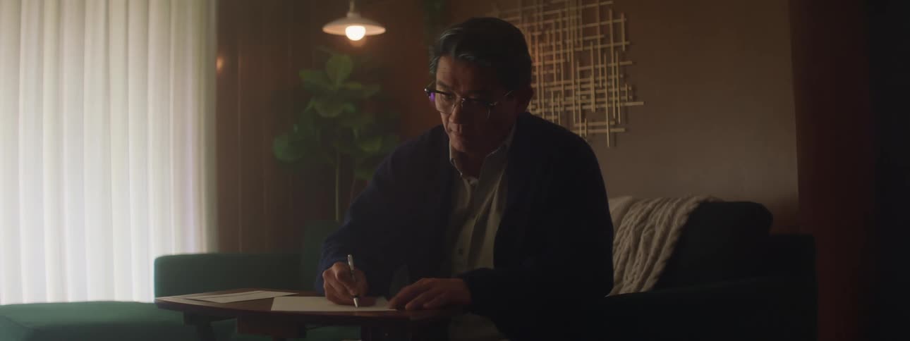 A man using a table to write on paper while sitting on a couch