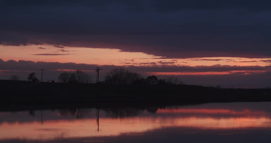 Pink and orange sunset reflecting off of a body of water with the silhouette of the tree lines as well