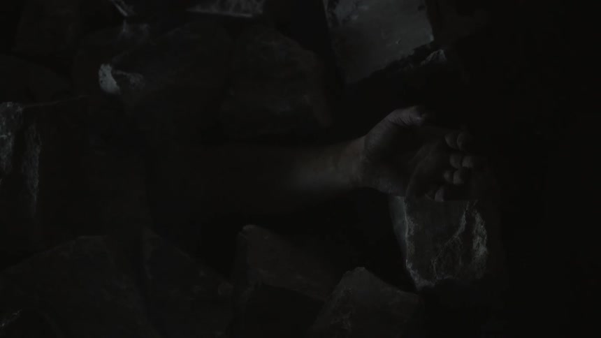 The arm of a person buried under smoky rubble