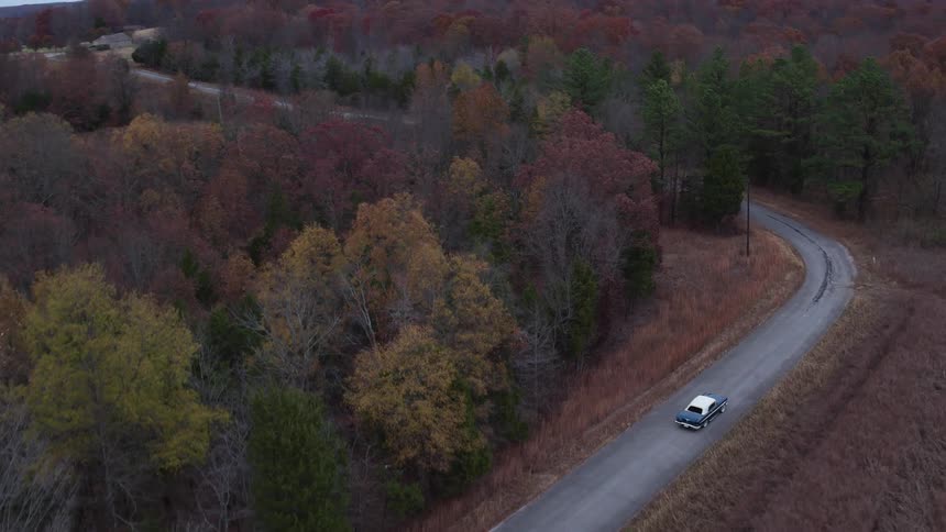 A car drives down a road surrounded by trees below