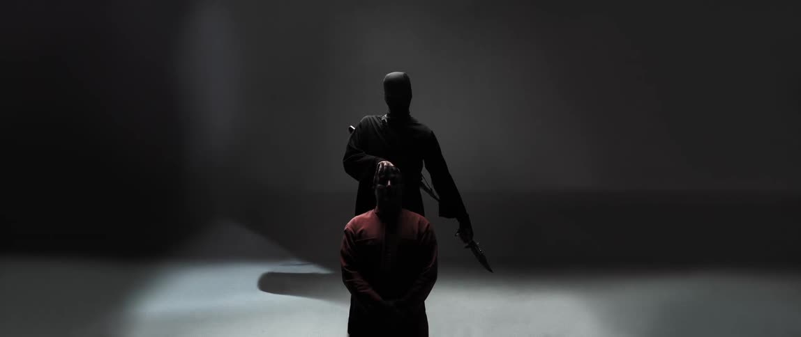 A man pulls a kneeling persons head back