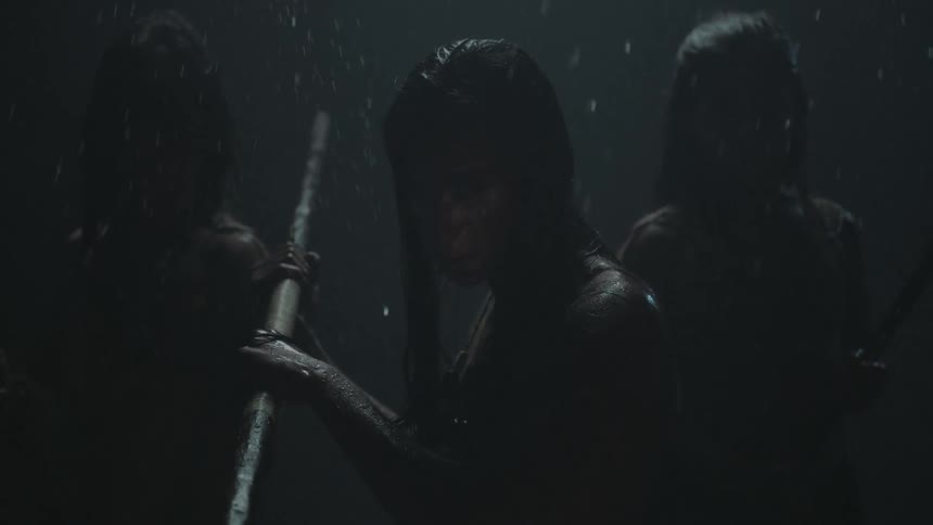 Three people are holding weapons as it rains in the dark