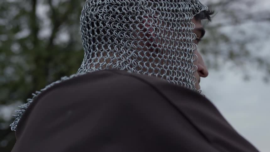 A man wearing a mesh metal head covering takes off his metal helmet