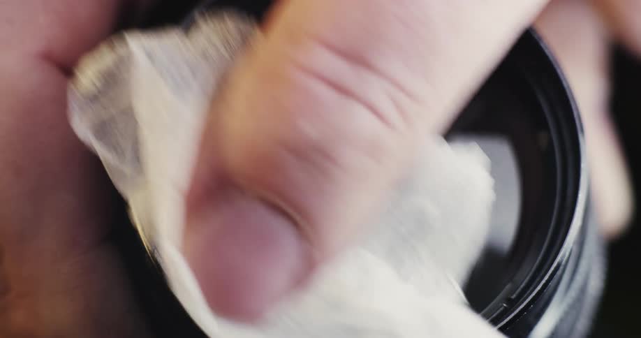 A person using a wipe to clean a glass lens
