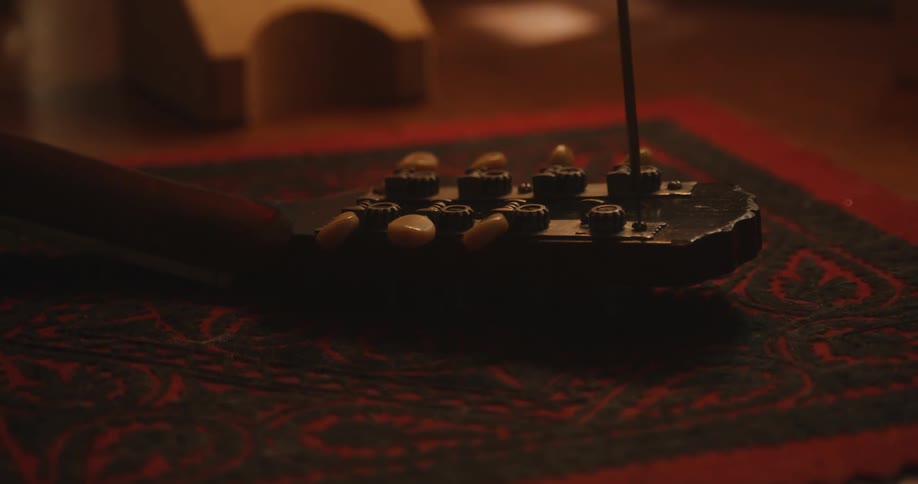 A person places a guitar head on a rug and uses a tool to manipulate the guitar