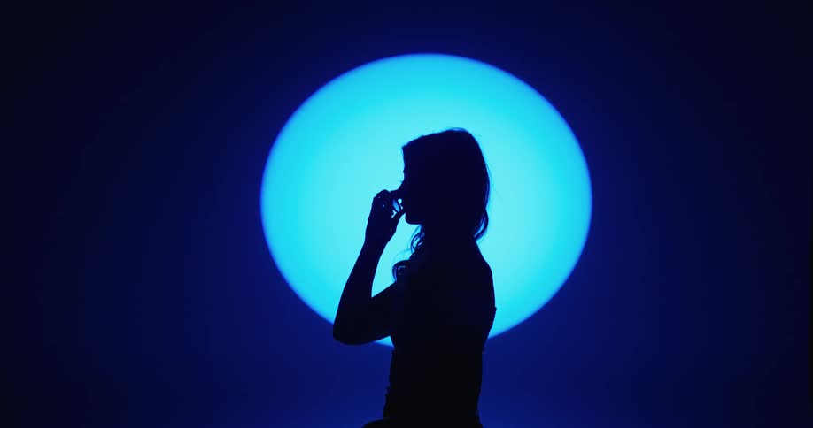 Female model with wavy hair taking off her sunglasses is silhouetted agains the spotlight in the studio