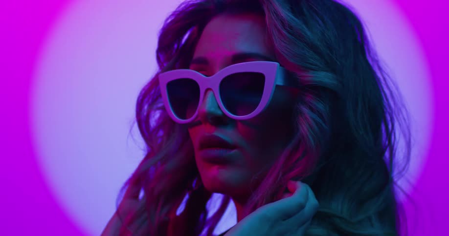 Young beautiful woman fluffs her curly long hair with her hands under magenta lights